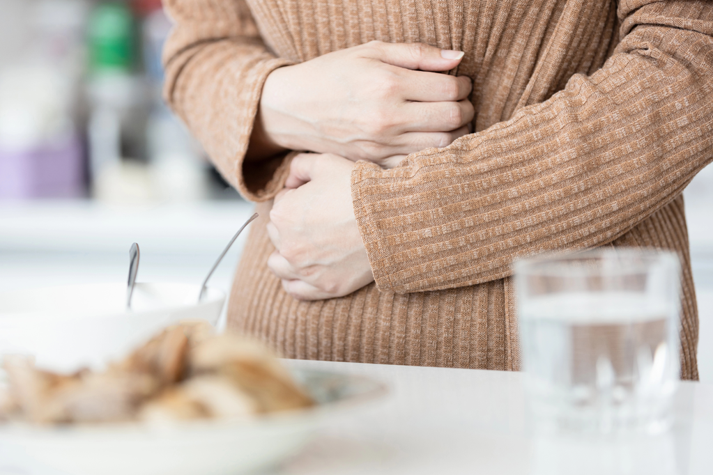 Person at the kitchen table clutching her stomach.